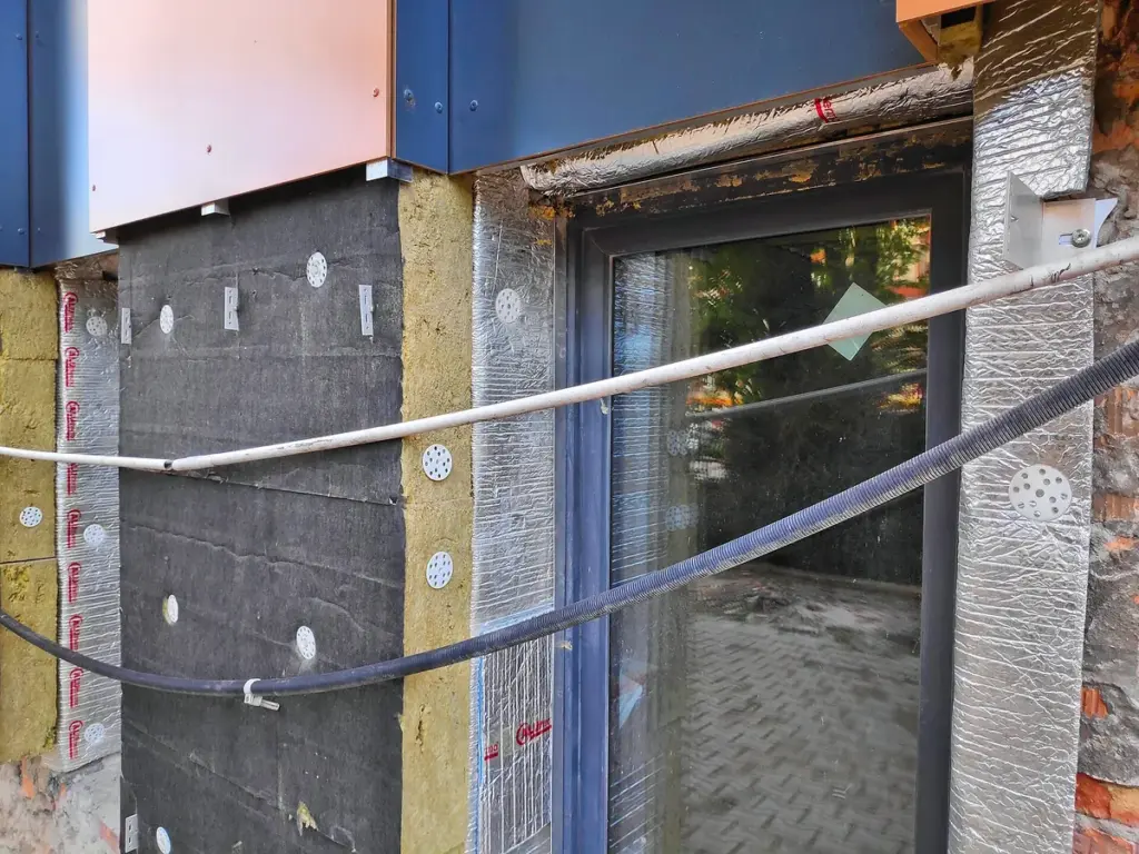 Fachada em obra recebendo placas de isolamento térmico presas com buchas