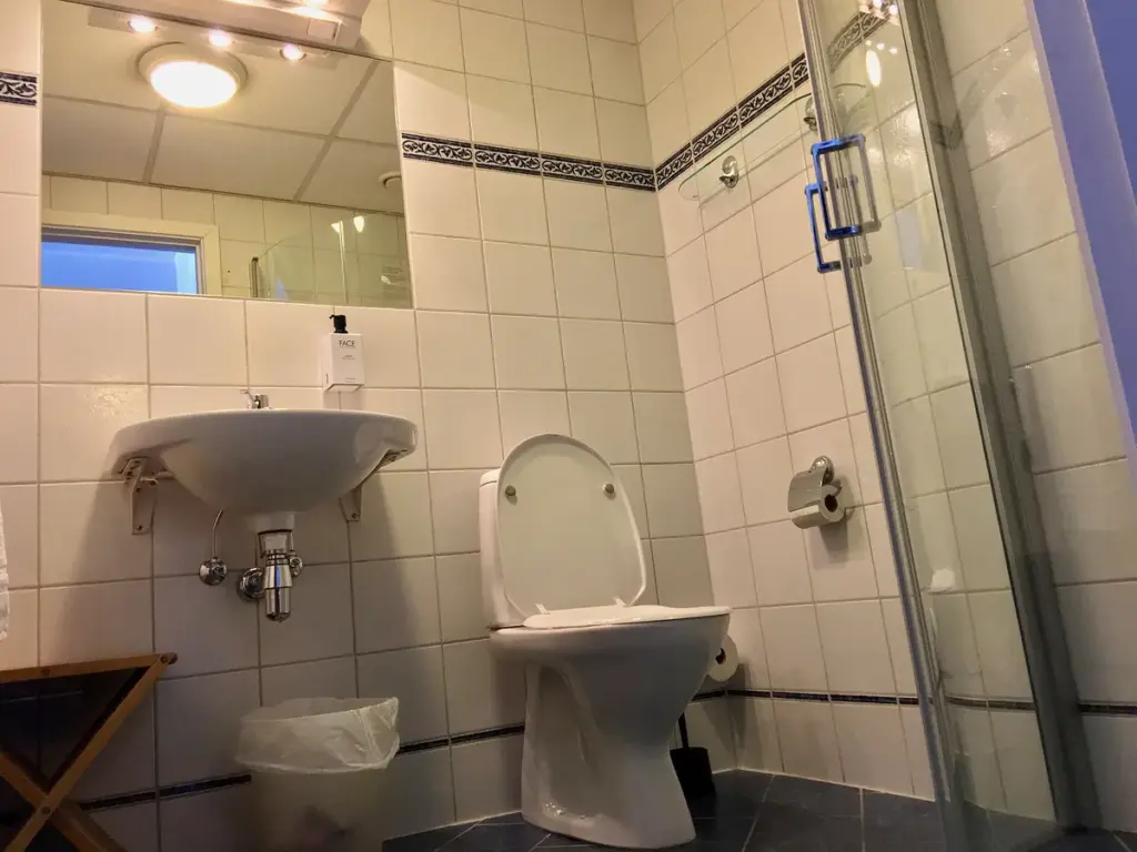 Banheiro revestido de azulejos brancos com vaso, pia e piso de cerâmica