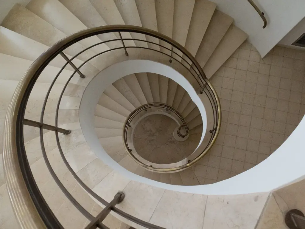 Escada em caracol branca vista de cima, com o corrimão acompanhando a espiral