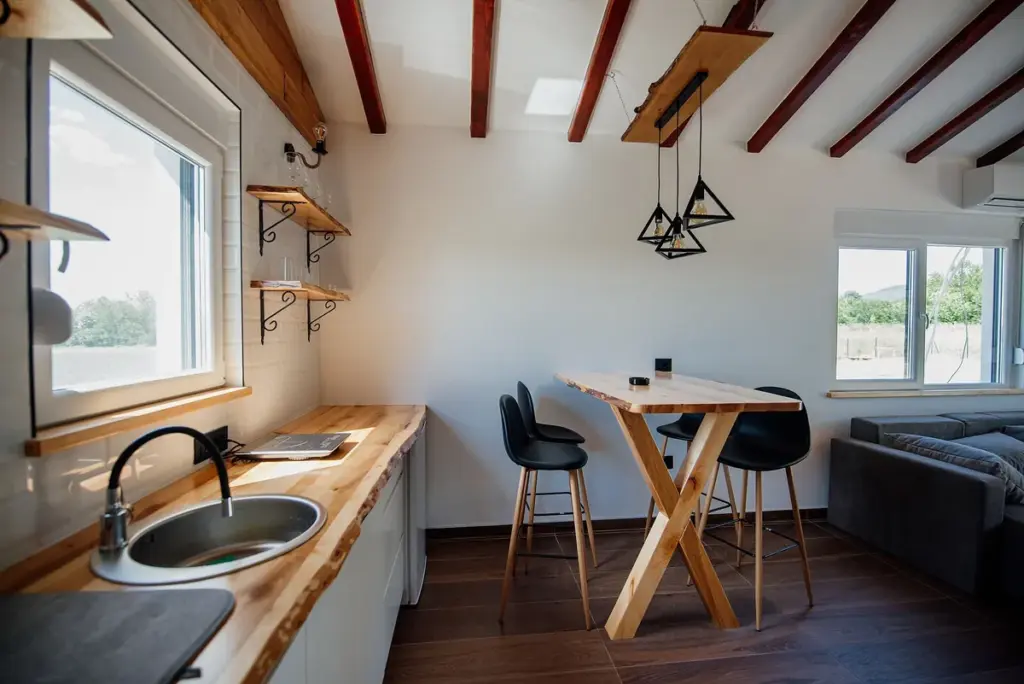 Cozinha com bancada de madeira, prateleiras abertas e luminárias pendentes sobre a mesa