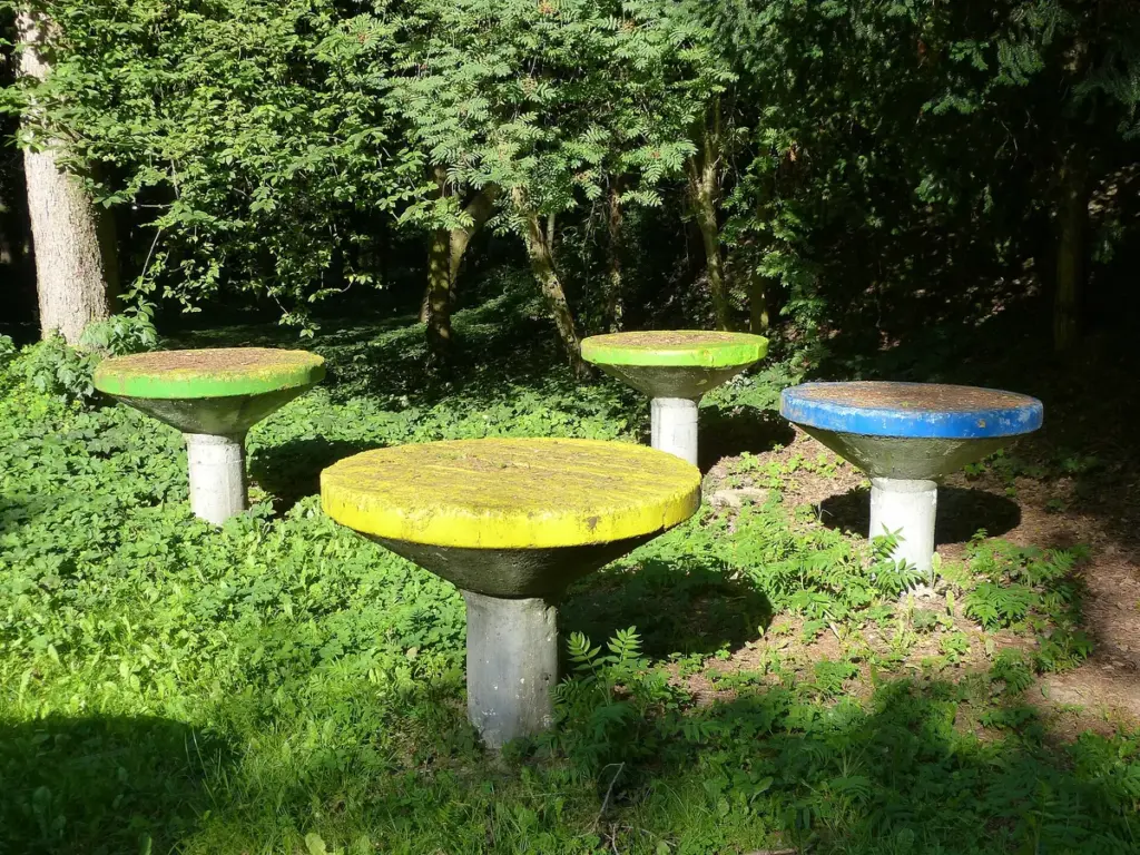Mesas de concreto coloridas em forma de cogumelo sobre o gramado de um parque